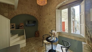 A rustic room with a stone wall, a round table with chairs, a hanging light fixture, and a window with shutters. - DOMUS GABRIEL (Giovinazzo)