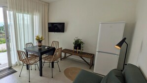 Ett modernt vardagsrum med en matplats, en platt-TV som är monterad på väggen, ett kylskåp och en soffa.