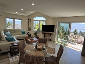 A living room with a sofa, coffee table, TV, and dining area with chairs and a table. - Lakeview Escape on Mount Boucherie (West Kelowna)