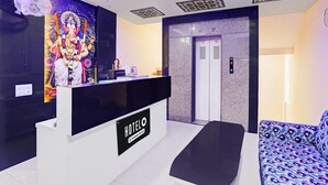 A hotel reception area with a reception desk, a sofa, an elevator, and a wall with a colorful mural. - Classic With Balcony Yug Residency (Varanasi)