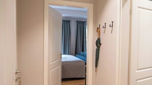 A hallway with wooden flooring, a bed with a grey duvet, and a coat hanging on the wall. - East Frisian chic: holiday home in country house with private lake (Friedeburg)