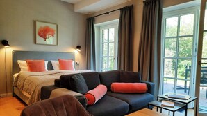 A bedroom with a bed, a sofa, a table, and a window with curtains. - East Frisian chic: holiday home in country house with private lake (Friedeburg)
