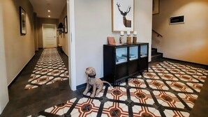 A hallway with patterned flooring, a framed deer antler artwork, a small dog statue, and a black console with glass doors. - East Frisian chic: holiday home in country house with private lake (Friedeburg)
