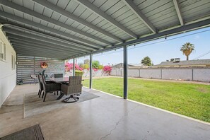 A covered patio with a table and chairs, a concrete floor, and a view of a grassy yard. - Copper Cactus | 3BR • Relaxing Backyard • Sleeps 6 (Scottsdale)