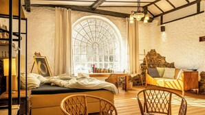 Ein gemütliches Zimmer mit einem Bett, einem Holzstuhl, einer Couch, einem großen Bogenfenster und einer Steinwand.