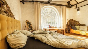 Ein Zimmer mit einem Bett, einem Tisch mit Büchern, einem Fenster und einer Steinwand.