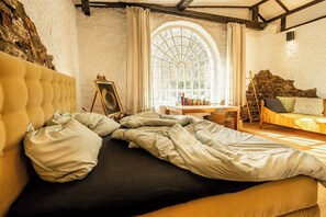 A room with a bed, a table with books, a window, and a stone wall. - Immerse yourself into the magic of this studio and discover your creative side (Kall)