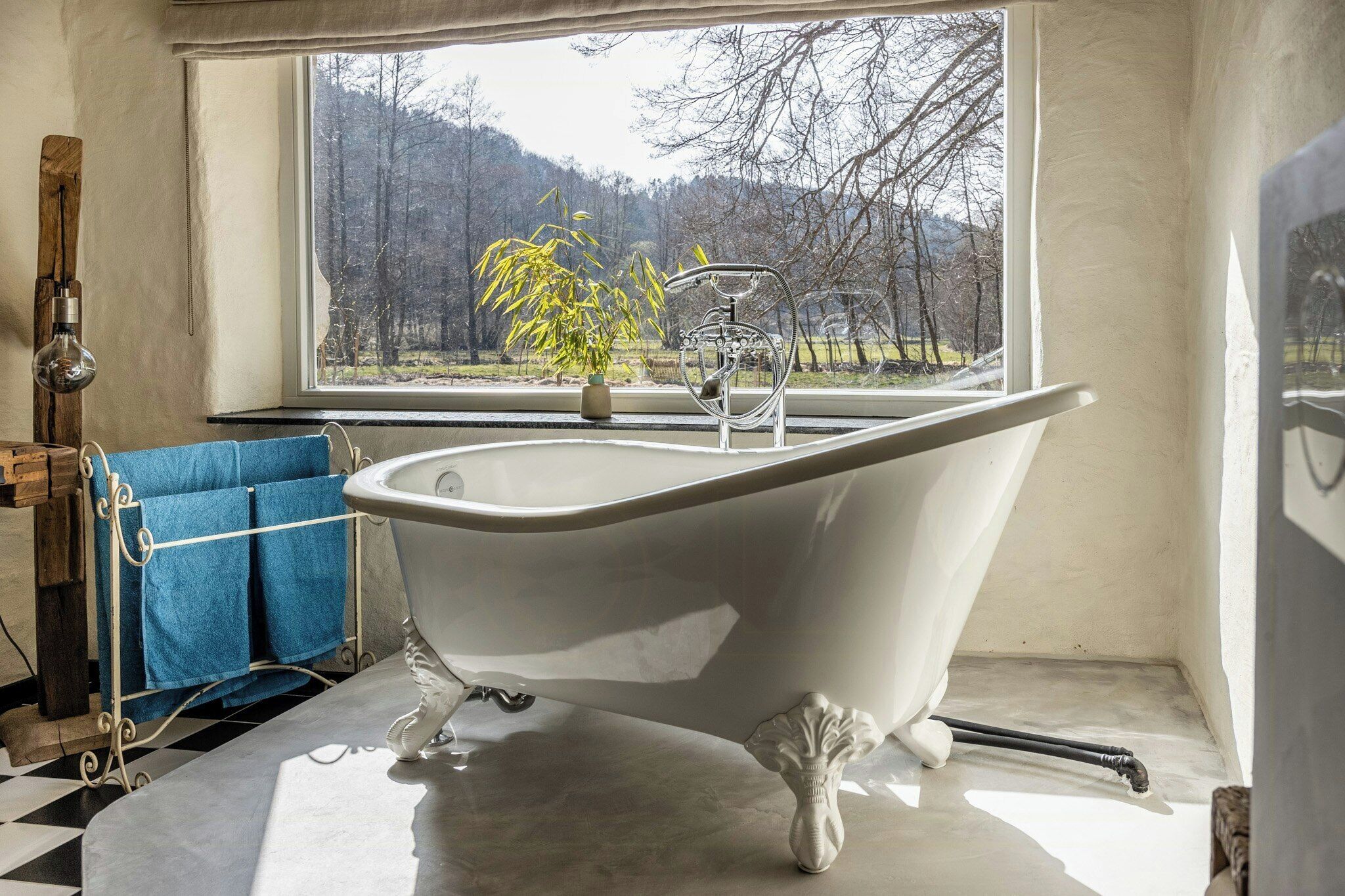 A bathroom with a bathtub, a window with a view of trees, and a towel rack with blue towels.