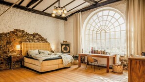 Ein Schlafzimmer mit Steinwand, einem Bett, einem Schreibtisch und einem großen Bogenfenster.
