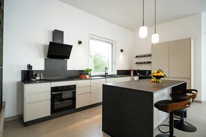Eine moderne Küche mit einer zentralen Kochinsel, integrierten Geräten und Pendelleuchten.