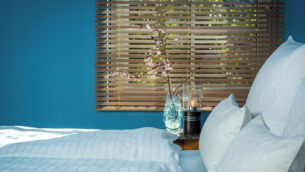 A bed with white linens, a vase with flowers, and a candle on a bedside table. - Stylish apartment Zander on the Eider river bend (Stapel)