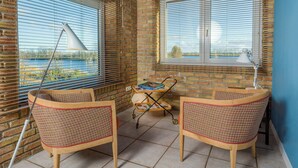 A room with a brick wall, two wicker chairs, a small table with a tray, and a window with blinds. - Stylish apartment Zander on the Eider river bend (Stapel)