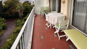 Ein Balkon mit Tisch und Stühlen, eine Schiebeglastür und Blick auf Grünflächen und eine Straße.