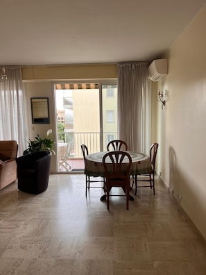 Un coin repas avec une table et des chaises, une plante en pot, un canapé et une porte-fenêtre coulissante donnant sur un balcon.