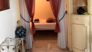 Ein Zimmer mit einem Bett, einer Lampe, einer Pflanze und einem Metallregal mit Gegenständen.