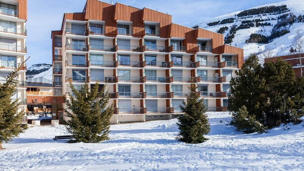 A multi-story hotel with a modern design, featuring balconies and a view of a snowy mountain. - Central Slope Stay for Four (Les Deux Alpes)