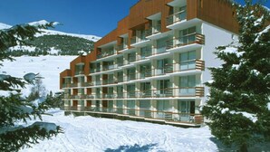 A multi-story hotel with balconies, set against a snowy mountain backdrop. - Central Slope Stay for Four (Les Deux Alpes)
