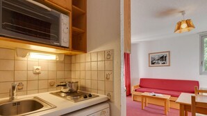 A compact kitchen with a microwave, stove, and dishwasher, leading to a living area with a red sofa and a dining table. - Central Slope Stay for Four (Les Deux Alpes)
