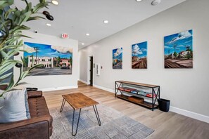 Un hall d’hôtel avec un canapé en cuir marron, une table basse en bois et une bibliothèque. Quatre tableaux représentant des scènes urbaines sont accrochés au mur.