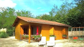 Une cabane en bois avec un toit en tuiles, une véranda avec des chaises et une balançoire.
