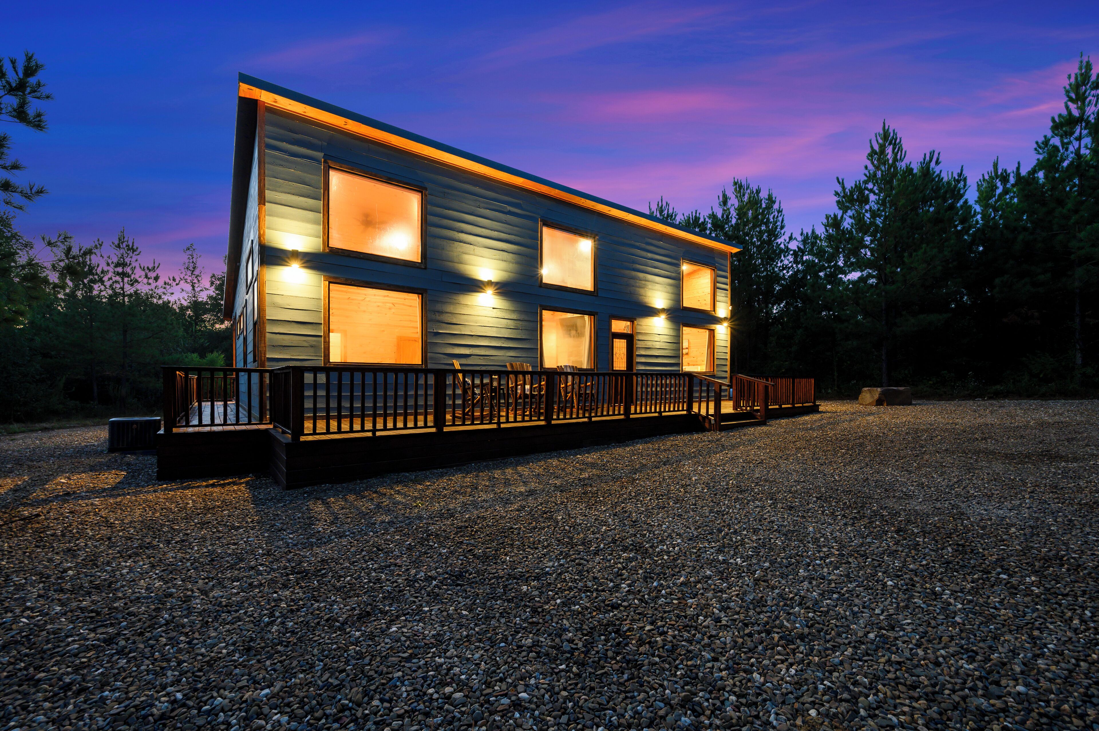 Un bâtiment moderne doté de nombreuses fenêtres, d’une allée en gravier et d’une clôture en bois.