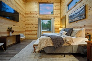 Ein Holzblockhaus-Interieur mit einem Bett, einem Schreibtisch und einem an der Wand befestigten Fernseher.