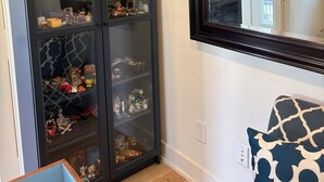 Une pièce comprenant un grand meuble vitré rempli de divers objets, un miroir au mur et un coussin à motifs sur une chaise.