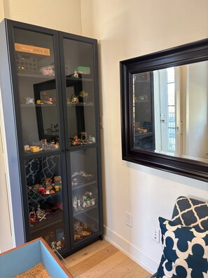 A room with a large glass-fronted cabinet filled with various items, a mirror on the wall, and a patterned pillow on a chair. - Modern Living in the Heart of the Action Downtown Arlington (Arlington)
