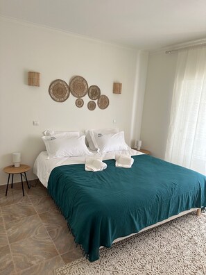 A neatly made bed with a teal bedspread, white pillows, and a decorative wall hanging. - BRANDA VILLA - Pool 10 min walk from the beach, right in the heart of Albufeira. (Albufeira)