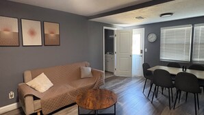 Ein Wohnzimmer mit Sofa, Couchtisch, Esstisch mit Stühlen und Bildern an der Wand.