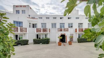 Un edificio moderno con varios balcones, una entrada central y follaje circundante.