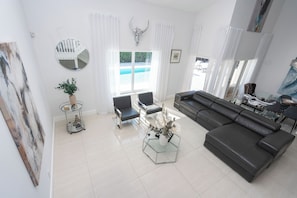A modern living room with a sofa, chairs, a coffee table, and a large window with curtains. - Beautiful Vacation home with Pool (Hialeah)