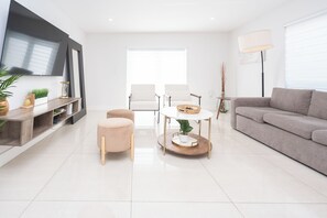 A modern living room with a sofa, two armchairs, a coffee table, a TV, and a lamp. - Beautiful Vacation home with Pool (Hialeah)