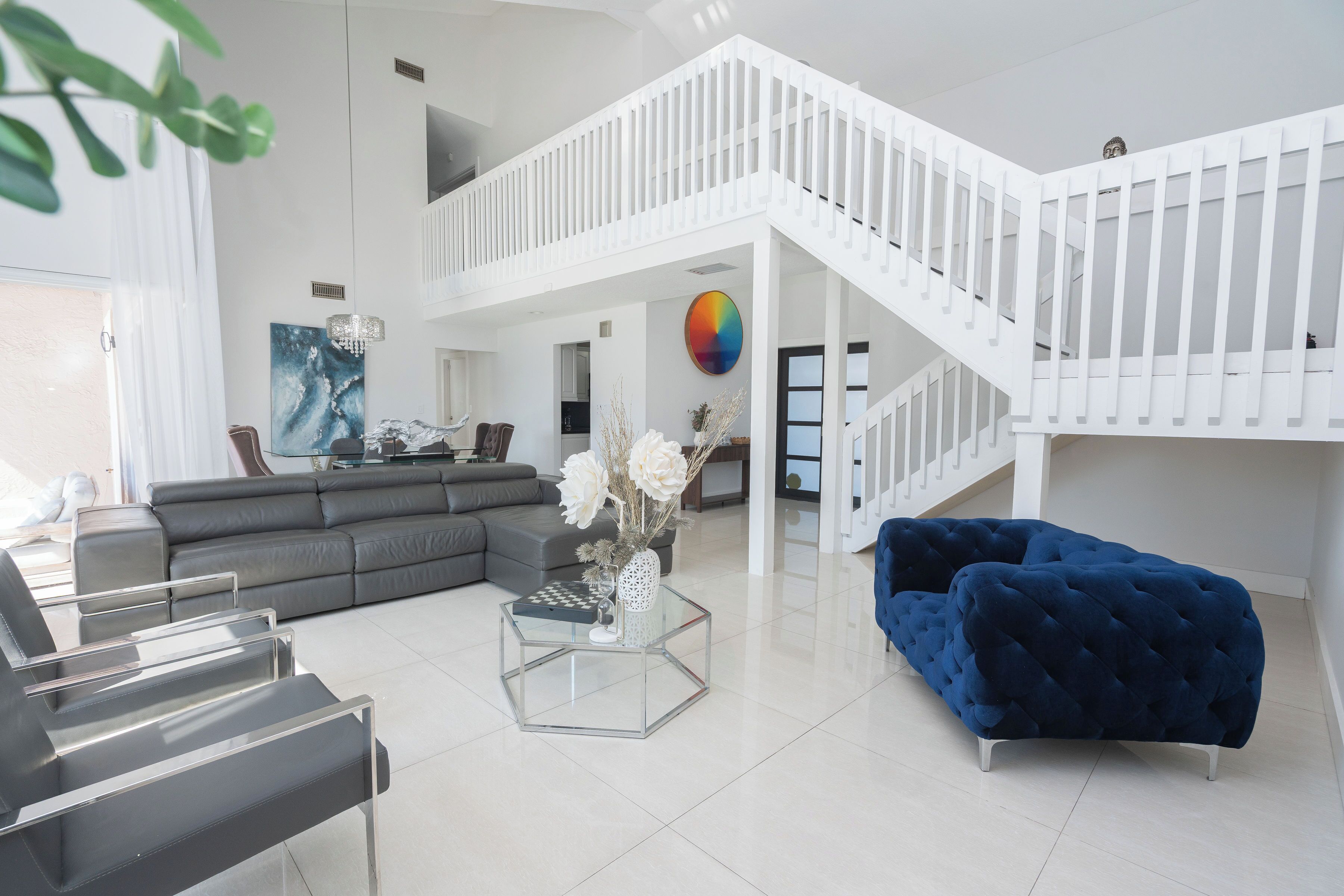 Un salon moderne avec un canapé d’angle, une table basse en verre, un canapé en velours bleu et un escalier blanc.