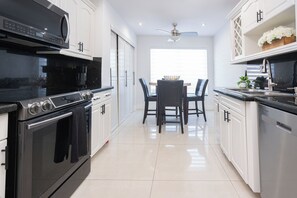A modern kitchen with a dining area, stainless steel appliances, and white cabinetry. - Beautiful Vacation home with Pool (Hialeah)