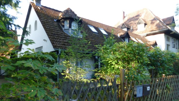 Une maison traditionnelle avec un toit en pente, une clôture en bois et un jardin où poussent différentes espèces de plantes.
