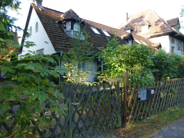 A traditional house with a sloped roof, a wooden fence, and a garden with various plants.