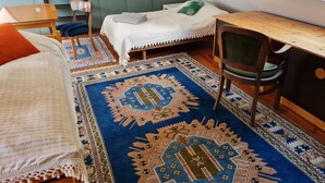 Une chambre à coucher aménagée dans un espace mansardé, avec un plafond en pente, un lit recouvert d’une courtepointe blanche, un bureau avec une chaise et une grande fenêtre.