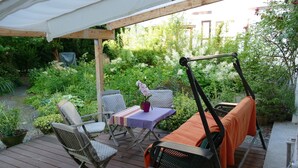 Une terrasse en bois, agréée de mobilier d’extérieur, notamment des chaises et une table, et entourée d’une végétation luxuriante.