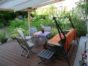 A wooden deck with outdoor furniture, including chairs and a table, surrounded by lush greenery.