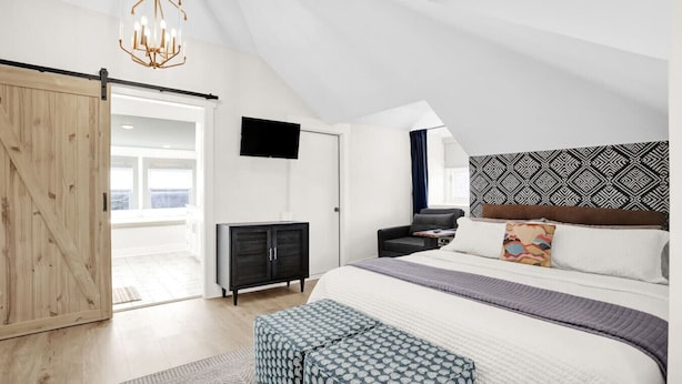A modern bedroom with a large bed, a TV, a wardrobe, and a sliding door to a balcony. - Walk to Memphis Nightlife | 100 Yr Old Cozy Apt (Memphis)