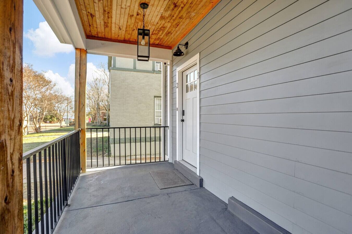 A covered porch with a wooden ceiling and a black metal railing.