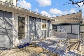 Un espace extérieur abrité avec une terrasse en bois et un tapis à motifs, une porte avec une sonnette et une fenêtre avec des stores.