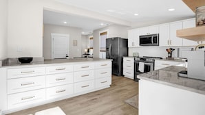 A modern kitchen with white cabinetry, a central island, stainless steel appliances, and a wooden floor. - Walk to Memphis Nightlife | 100 Yr Old Cozy Apt (Memphis)