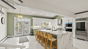 A modern kitchen with a marble island, wooden bar stools, stainless steel appliances, and a large window.