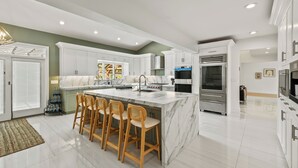 A modern kitchen with a marble island, wooden bar stools, stainless steel appliances, and a large window.