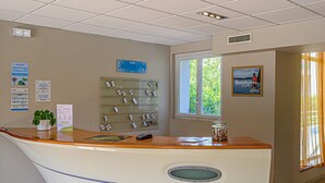 A reception desk with a plant, a bulletin board, and a window with greenery outside. - Studio With Balcony Near Vannes (Plescop)