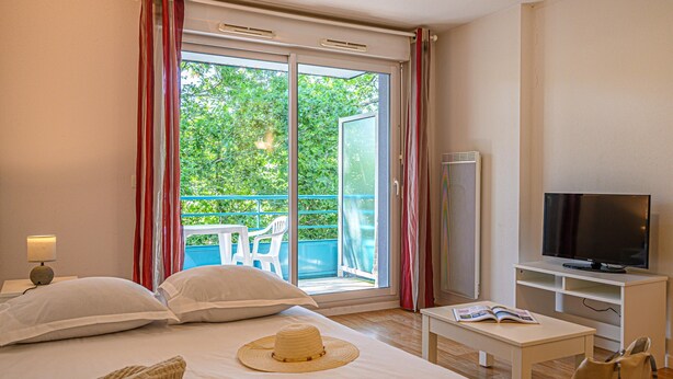 A hotel room with a bed, a television, a small table, and a balcony with a view of greenery. - Studio With Balcony Near Vannes (Plescop)
