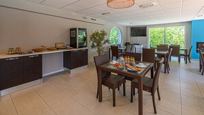 A modern kitchen with a dining area, featuring a large island, wicker furniture, and a television. - Studio With Balcony Near Vannes (Plescop)