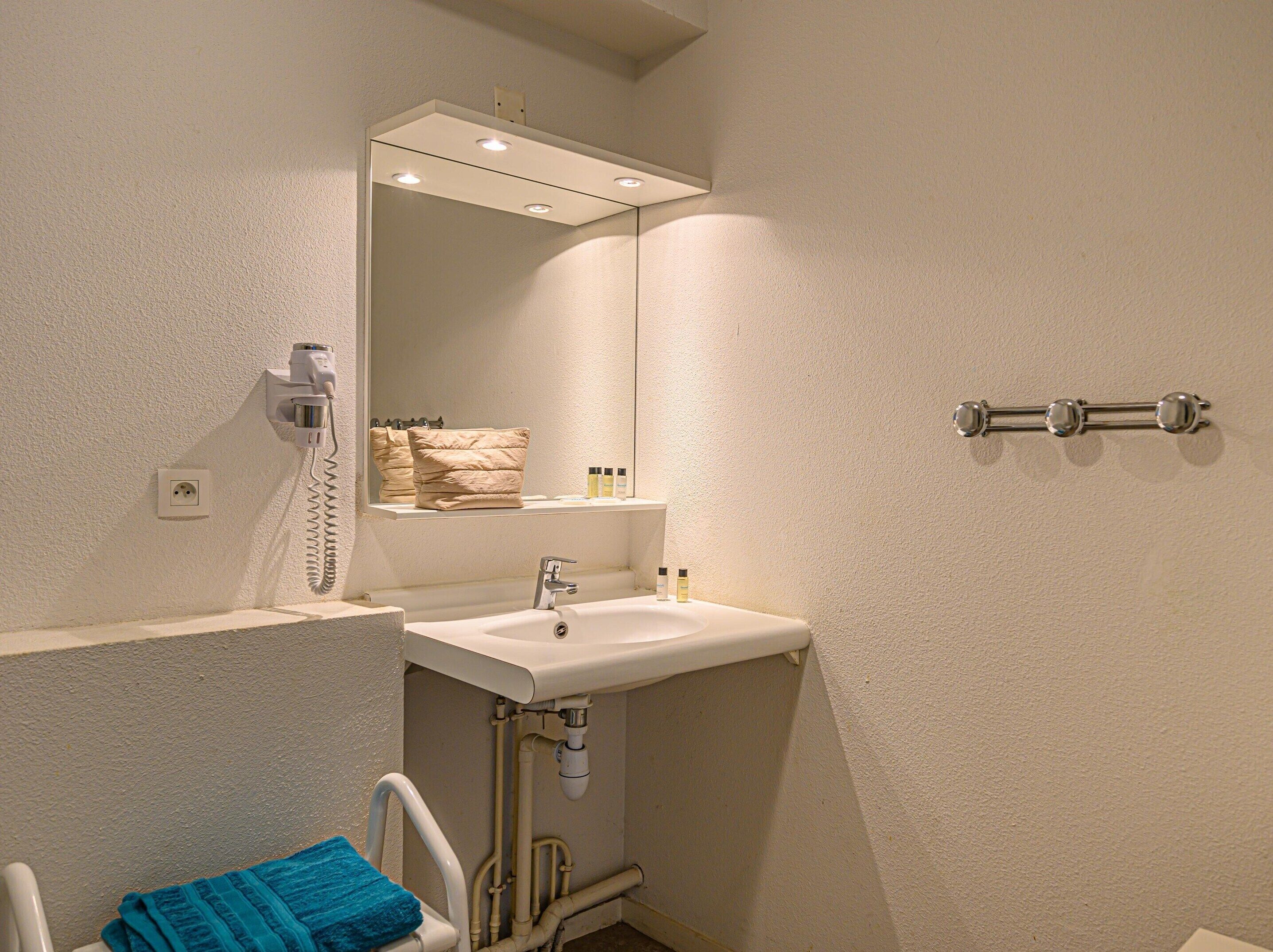 Un baño con lavamanos, espejo, toallero y barra de apoyo.